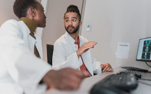 Man in a lab coat gesturing while talking with colleagues at a table